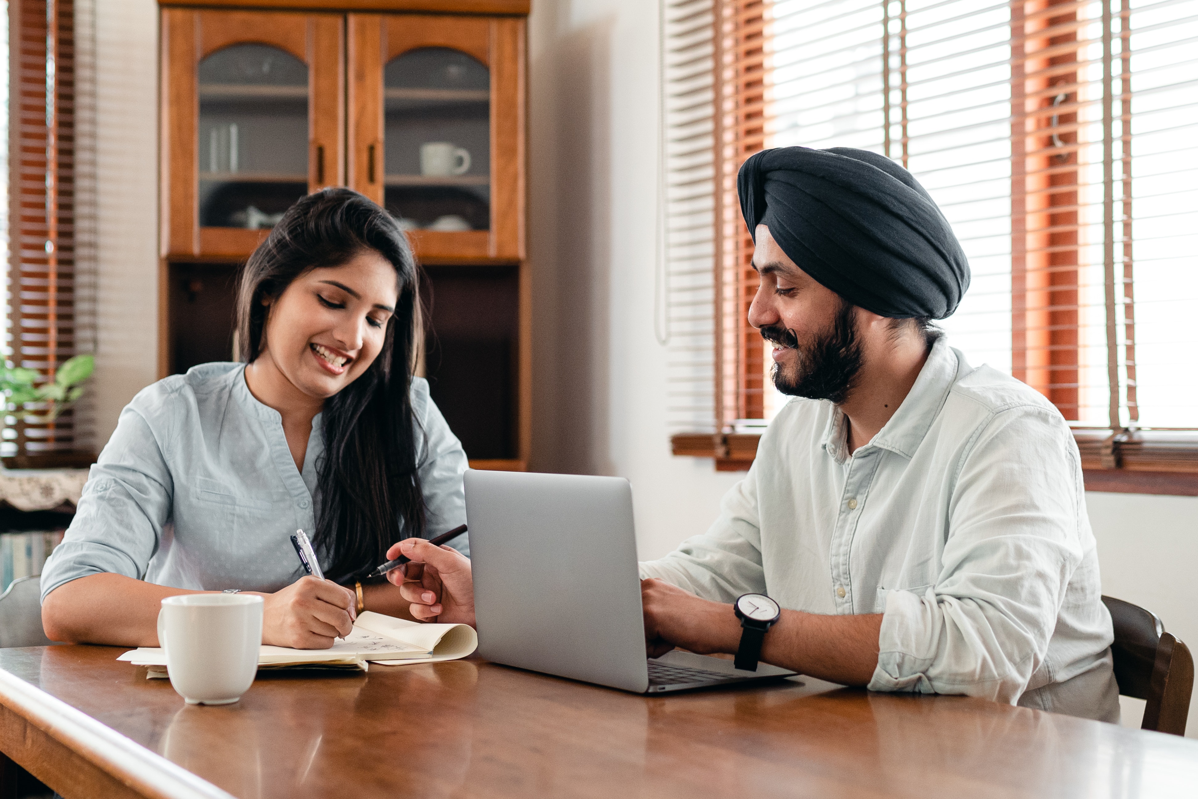 A man and a woman are smiling and working together at a desk with a laptop and paperwork